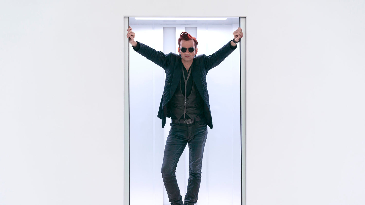 A photo of Crowley standing, his arms aloft, leaning against the doors of an elevator.