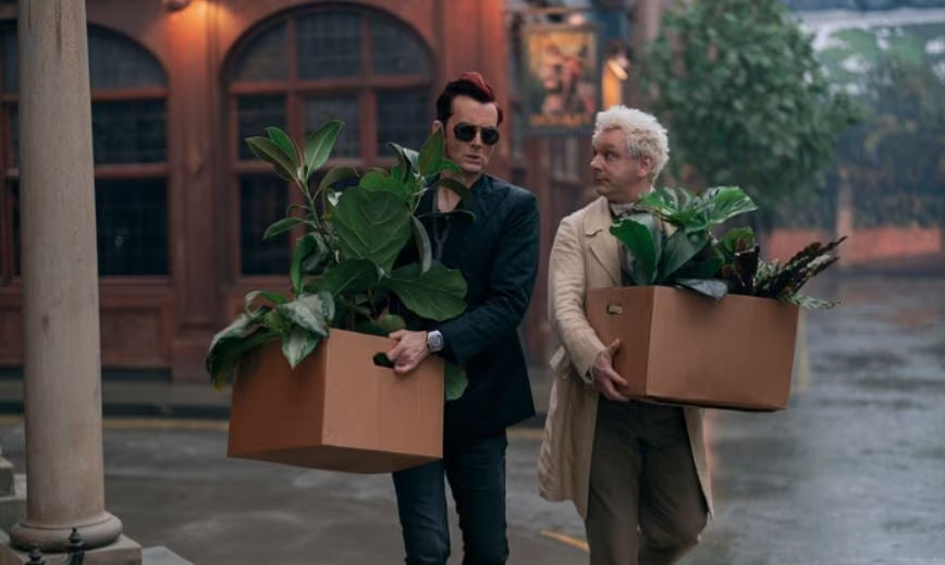 Crowley and Aziraphale carrying boxes full of plants.