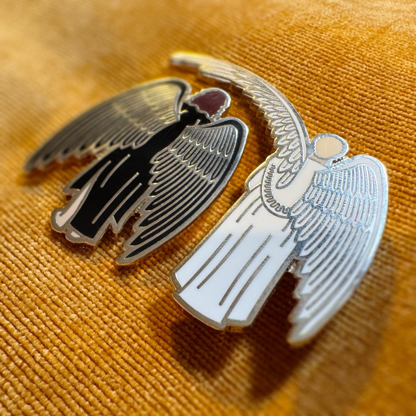 Photograph of Good Omens enamel pin against a fabric backdrop: Sheltering Wings.