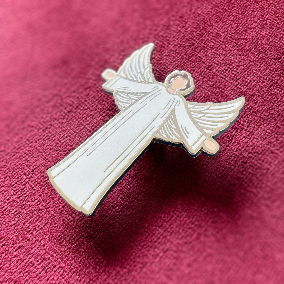 Photograph of a Good Omens enamel pin on a fabric background: Angelic Crowley