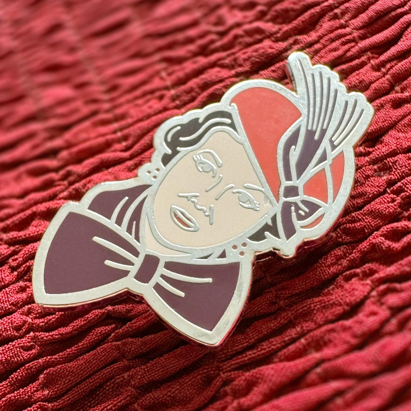Photograph of a Good Omens enamel pin on a fabric background: Shax