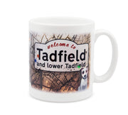 A white mug featuring an illustrated sign that says 'welcome to Tadfield and lower Tadfield'.